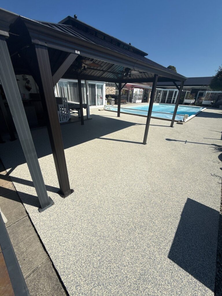 A modern backyard swimming pool featuring a slip-resistant, grey-colored polyurea pool deck coating by TSR Concrete Coatings.